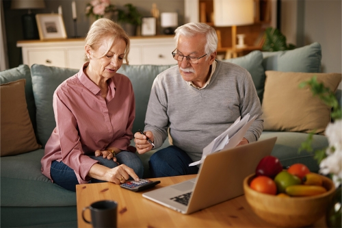 Rentnerehepaar sitzt auf Couch beim Laptop